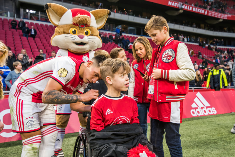 Ajax-mascotte en supporters langs het veld bij een thuiswedstrijd